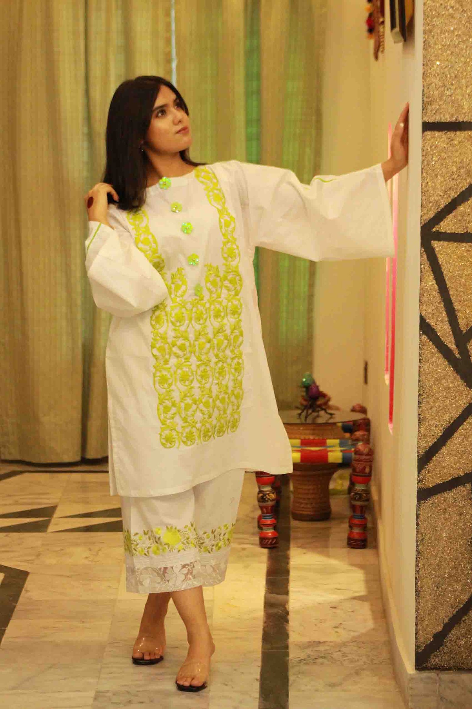 White tunic featuring vibrant lime green embroidery on the chest and matching floral embroidery on the hem of her cropped trousers.