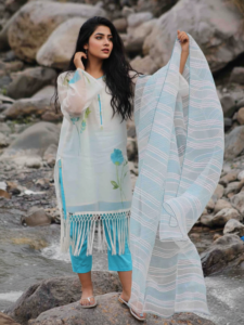 Azure Bloom Lawn Ensemble, a stunning 3-piece white lawn suit featuring vibrant turquoise floral hand-painted art, a long fringe hem, and a matching striped organza dupatta